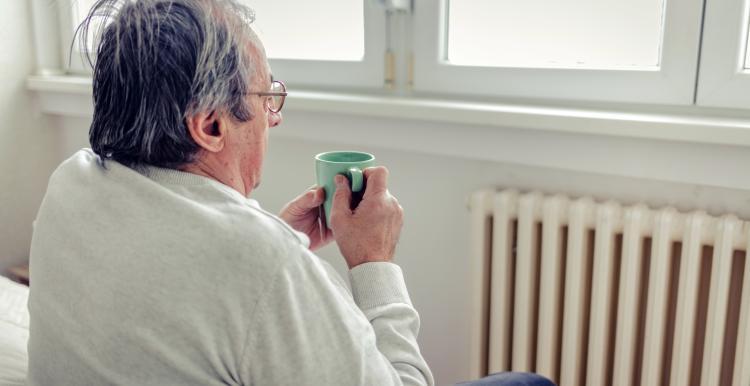 Man sits by radiator holding mug